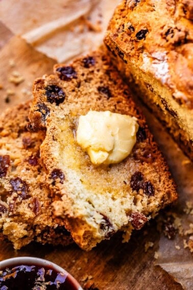 Crusty slice of Irish soda bread by larger loaf and small bowl of blackberry jam.
