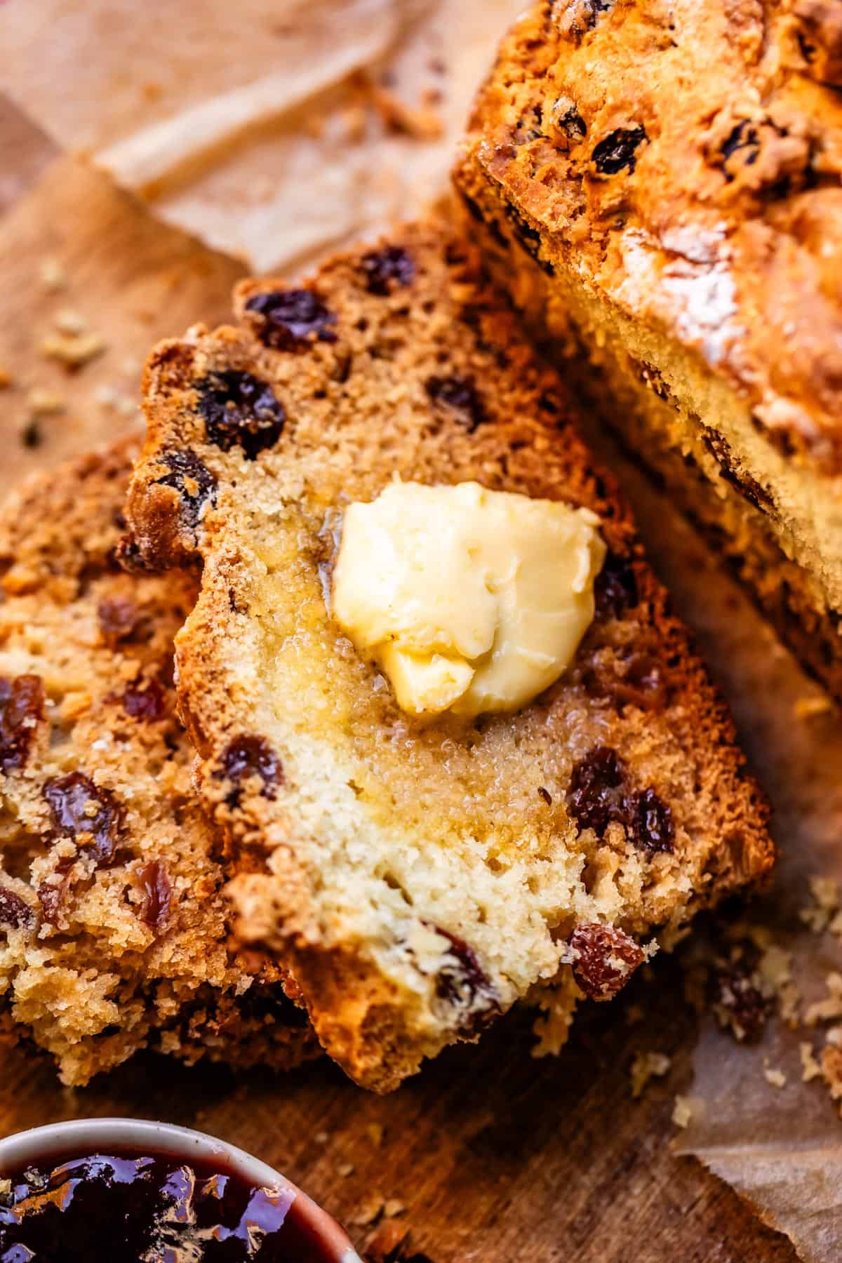 Crusty slice of Irish soda bread by larger loaf and small bowl of blackberry jam.