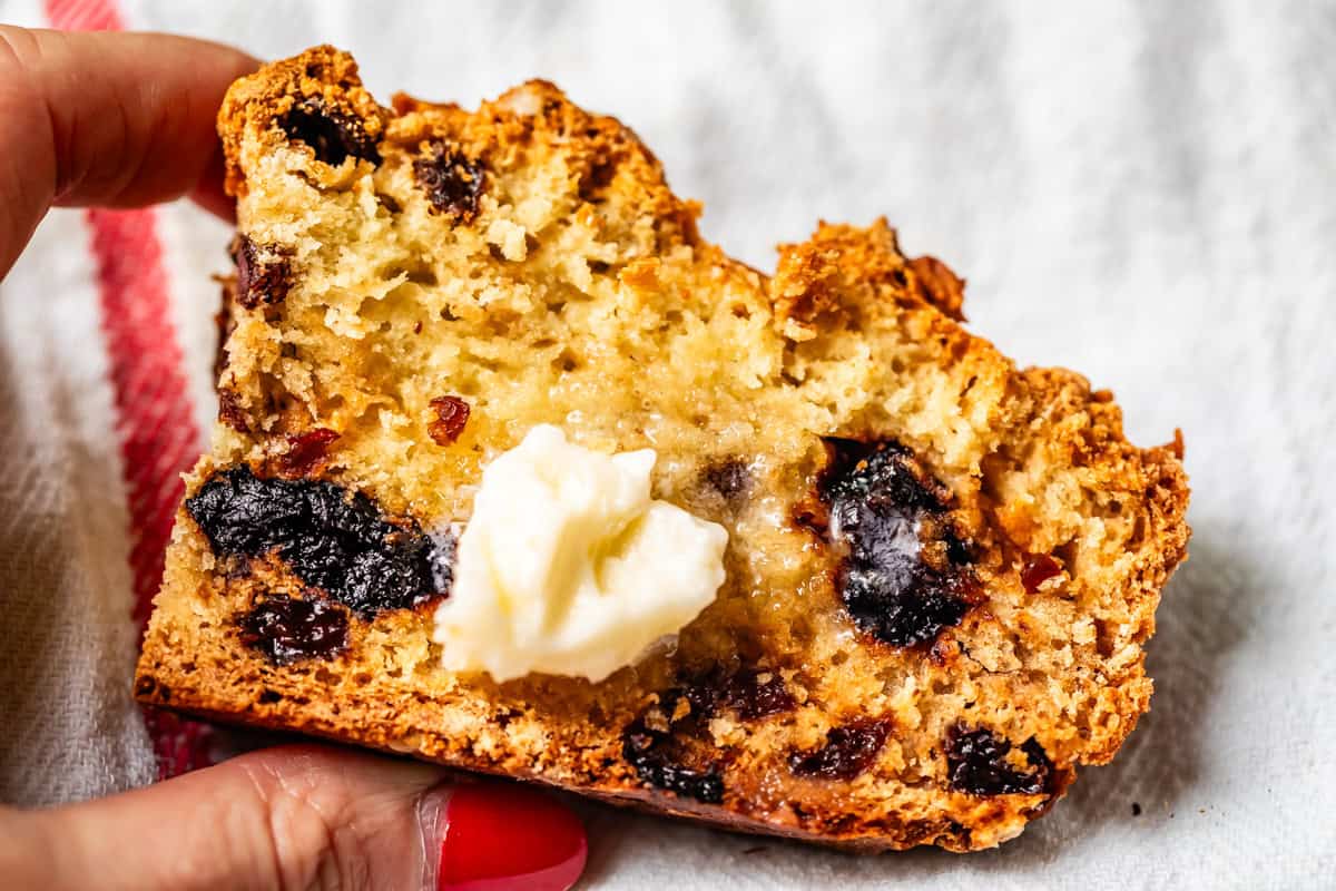 Close-up of soda bread showing baked-in cherries and raisin with pat of butter melting on the center.