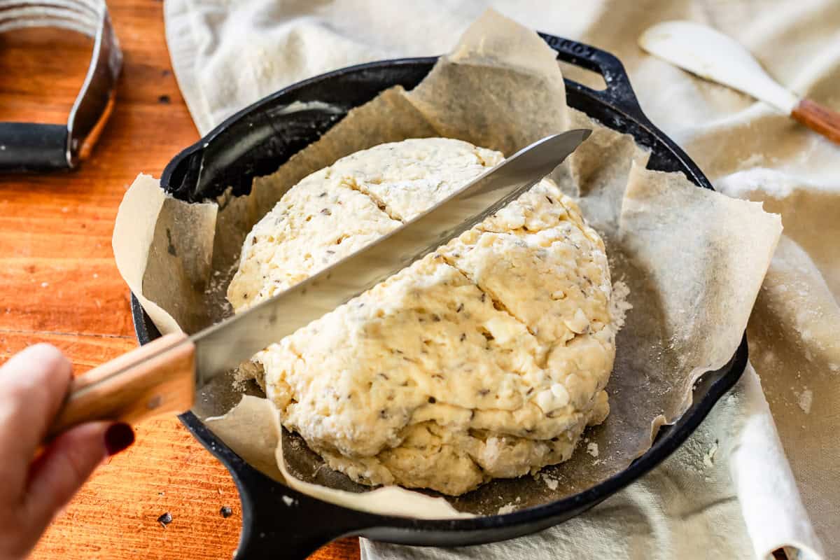 Slicing divots in the top of Irish soda bread dough before baking with bread knife in cast iron skillet.