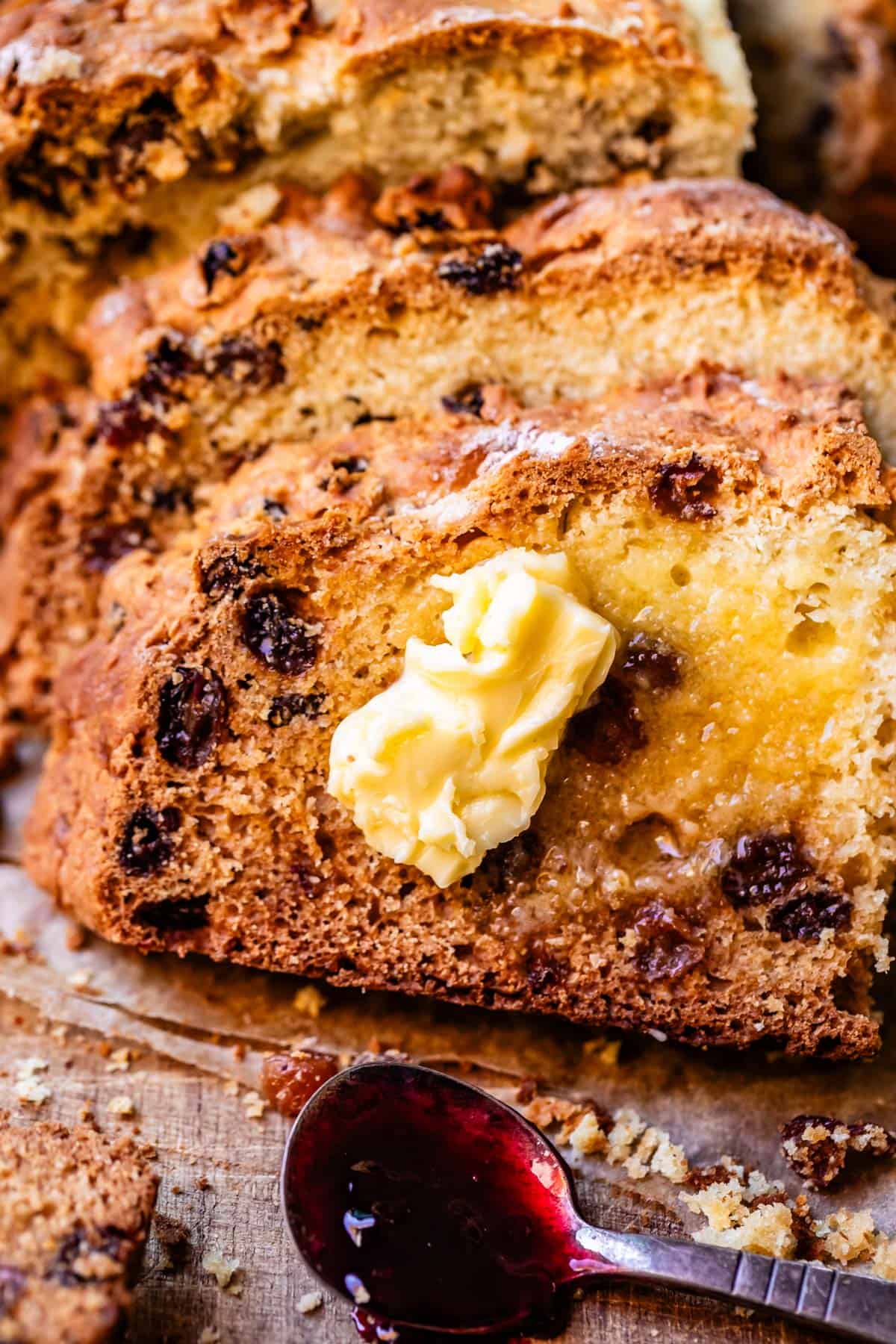 Irish soda bread slices leaning atop one another on cutting board with pat of butter on top and small spoon with blackberry jam.