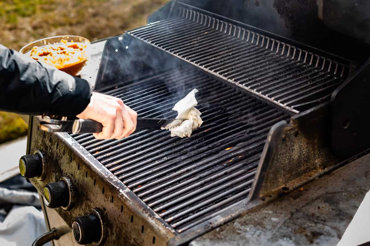 oiling grates of outdoor grill using a paper towel and tongs.