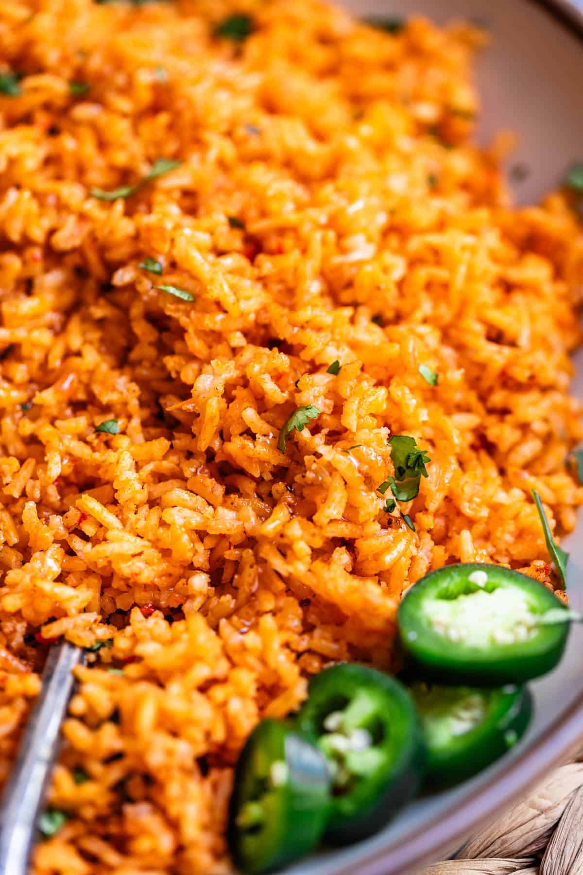 a spoon in a large serving of Mexican rice with jalapeno garnish.