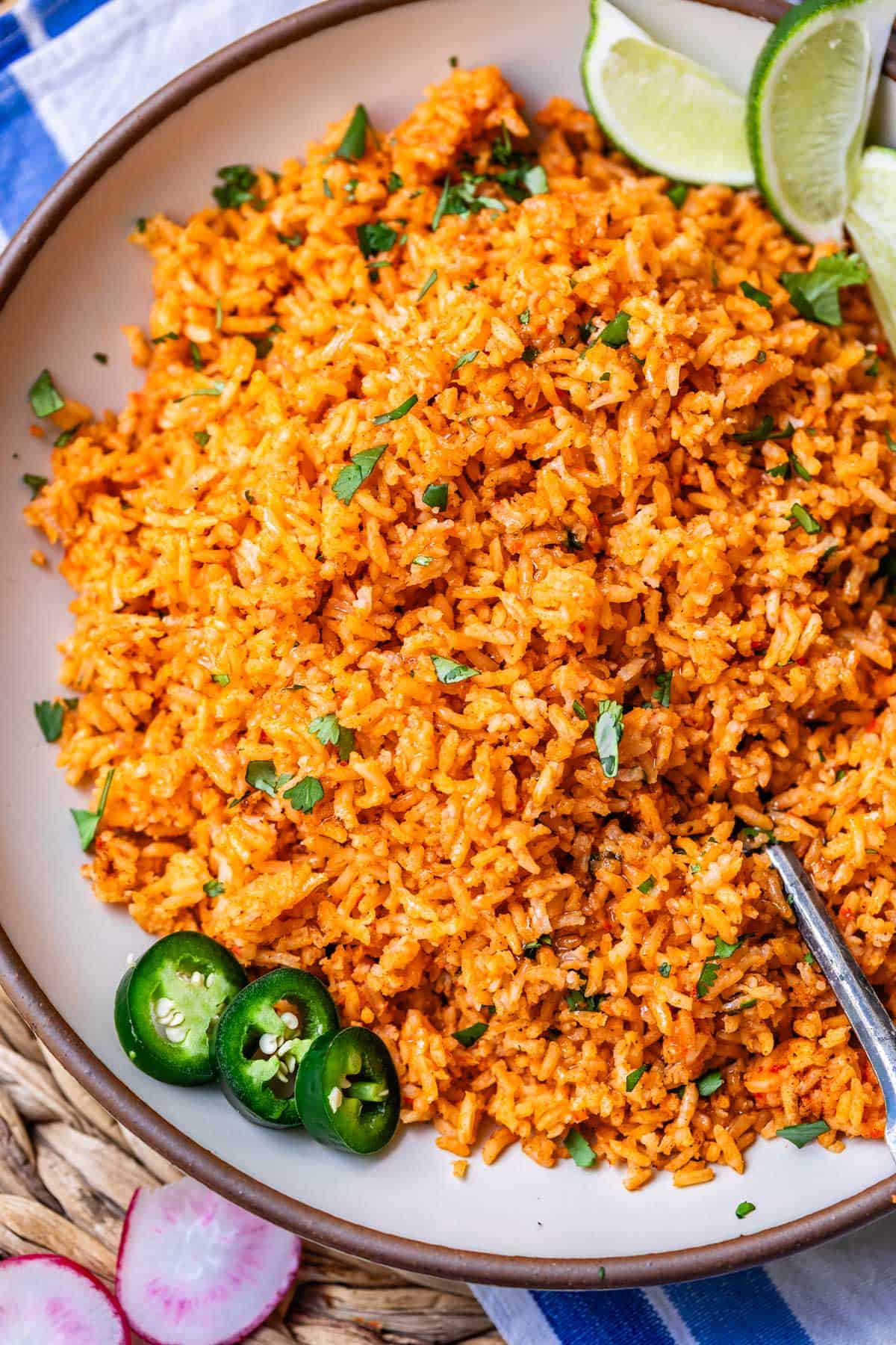 a round serving platter filled with Mexican rice and jalapeno, lime, and cilantro garnish.
