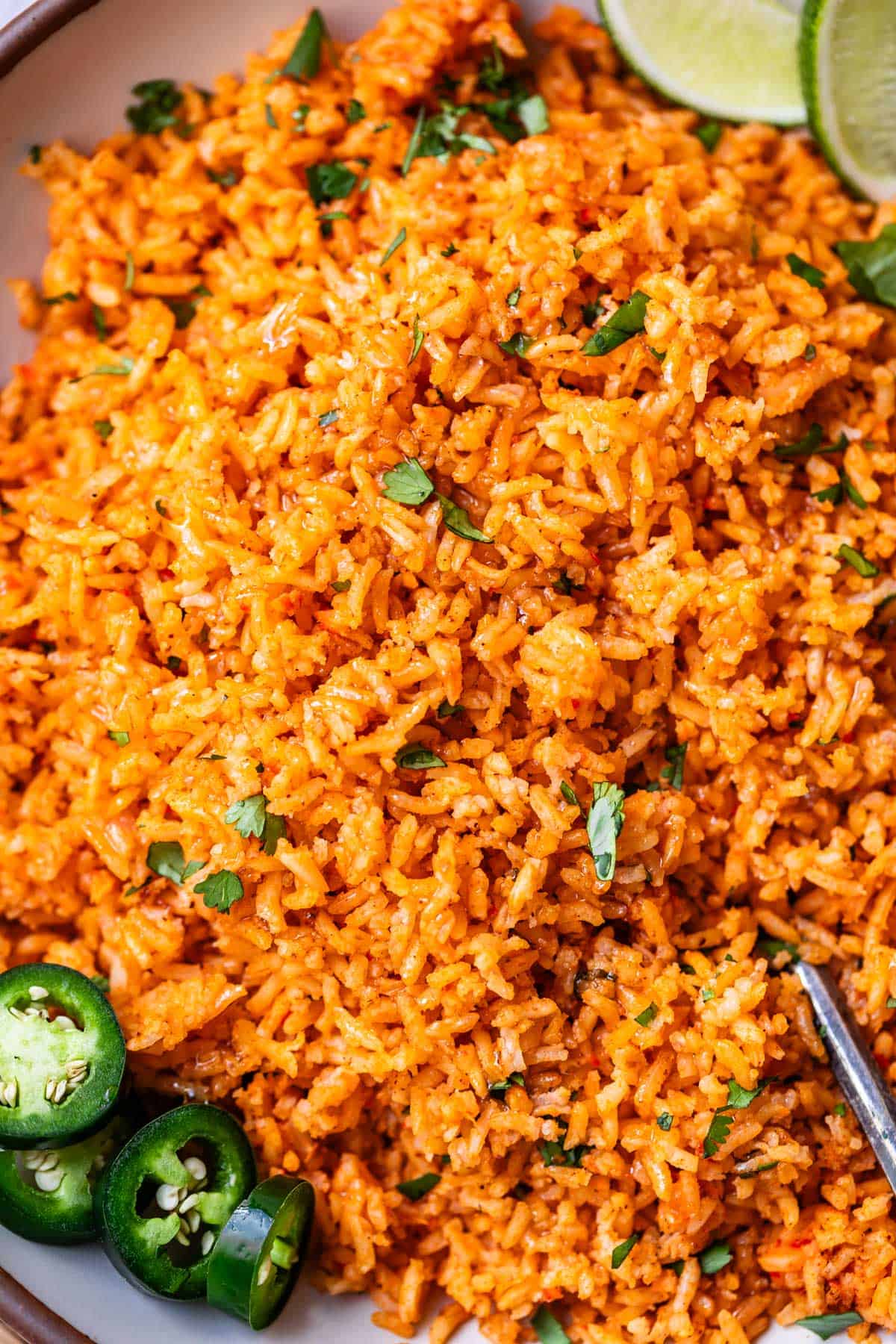 a spoon in a serving platter filled with Mexican rice and jalapeno and cilantro garnish.