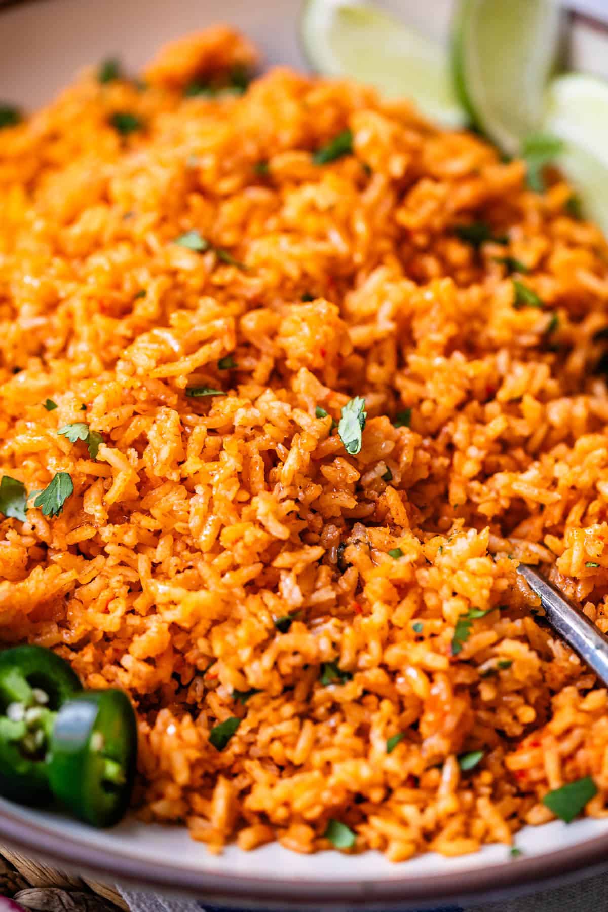 a spoon in a serving platter filled with Mexican rice and jalapeno and cilantro garnish.