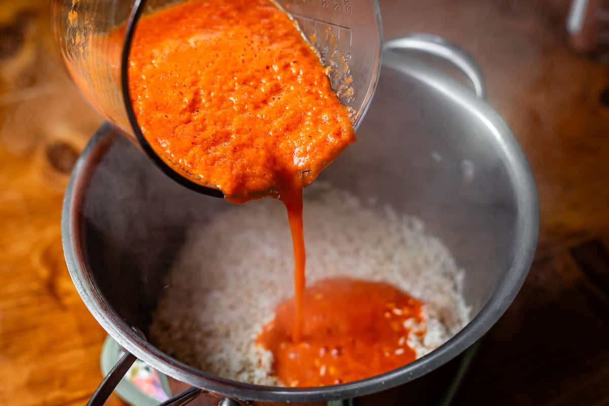 tomato sauce being poured from blender into metal pan with rice in it.