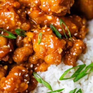 close up of white rice and crispy orange chicken with green onion garnish.