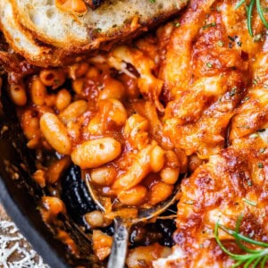 metal spoon and sourdough slice stuck into a cast iron skillet of cheesy beans.