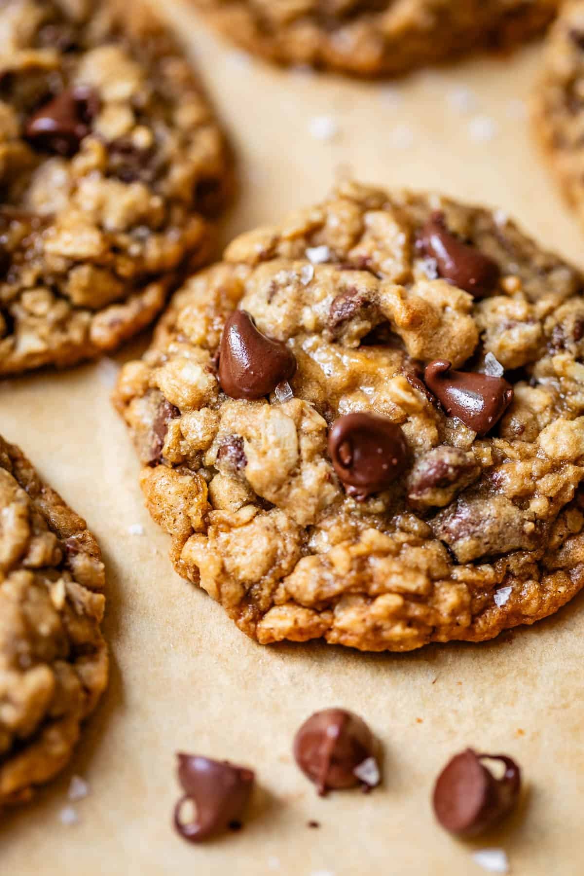 close up of some oatmeal chocolate chip cookies with flaky sea salt on parchment paper.