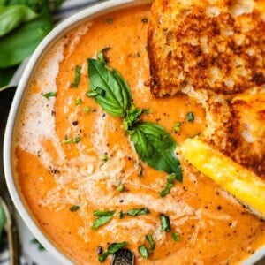 ceramic bowl of tomato bisque garnished with cream, basil, and grilled cheese.