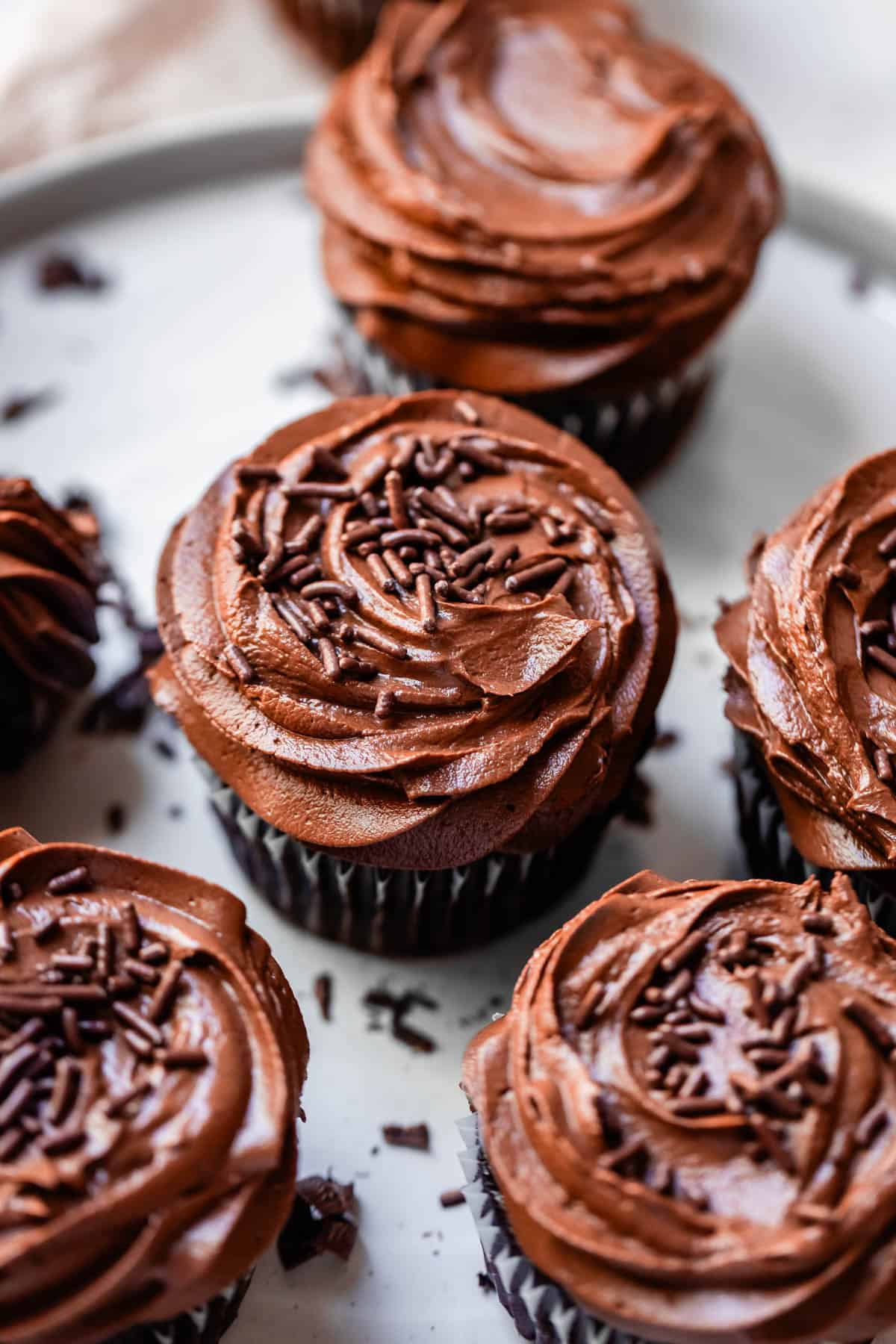 five chocolate cupcakes topped with chocolate buttercream and sprinkles on a tray.