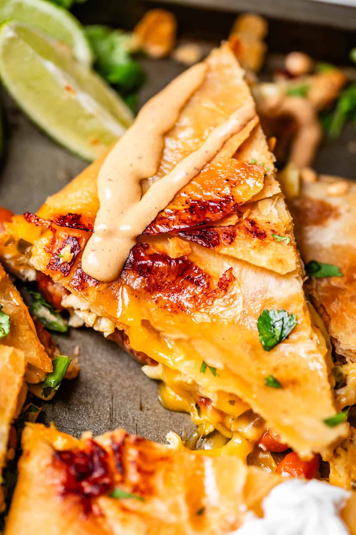 Close-up of a cheesy quesadilla slice topped with a creamy sauce, garnished with chopped herbs.