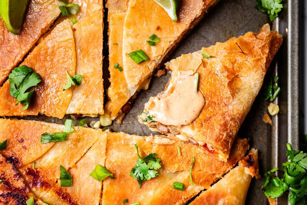 Close-up of crispy quesadilla slices topped with chopped green onions, cilantro, and a wedge of lime.