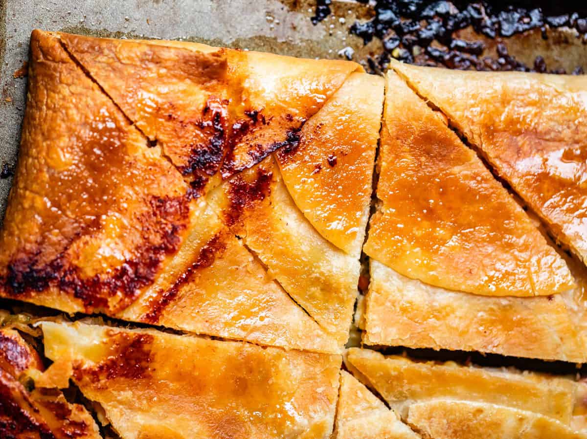Close-up of golden, flaky baked quesadillas cut into triangular pieces on a baking sheet.
