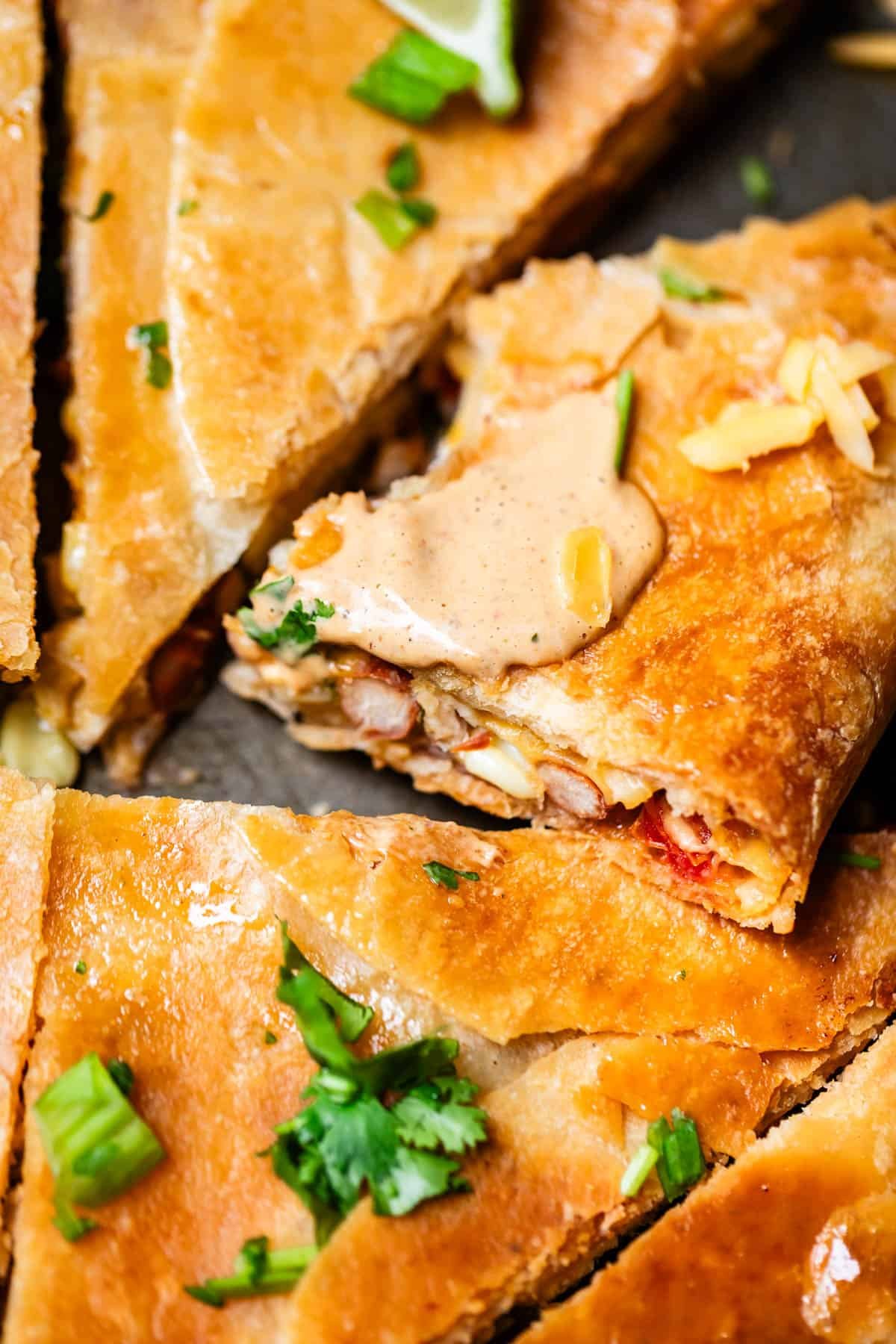 Close-up of golden, crispy quesadilla slices filled with beans and vegetables, topped with creamy sauce, melted cheese, and garnished with cilantro.