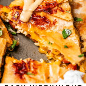 A close-up of cheesy sheet pan quesadilla slices topped with sauce and fresh herbs, with a lime wedge and sour cream on the side. Text reads: “Easy Weeknight Sheet Pan Quesadillas. The Food Charlatan.”.