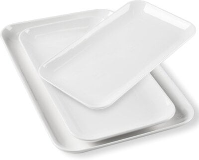 Three white porcelain rectangular serving trays of different sizes are stacked slightly askew on top of each other against a plain background.