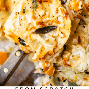 Close-up of a serving of butternut squash lasagna topped with melted cheese, herbs, and spinach, being lifted from a baking dish. Text at the bottom reads From Scratch Butternut Squash Lasagna The Food Charlatan.