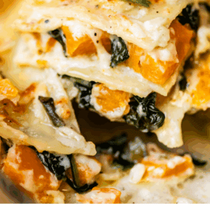 A close-up of creamy butternut squash lasagna with visible layers of pasta, orange squash, melted cheese, spinach, and a golden, bubbly top. Text below reads Butternut Squash Lasagna.