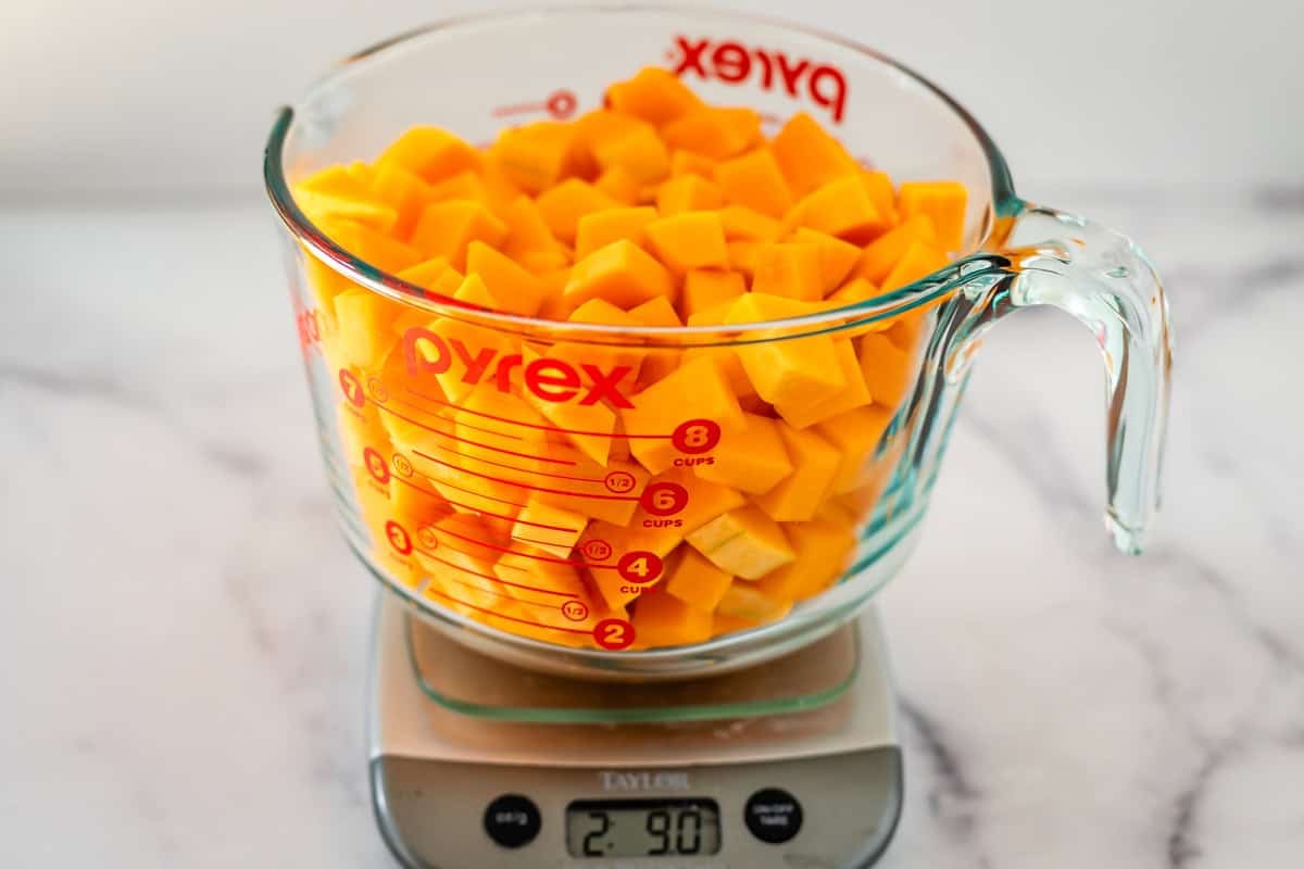 A glass Pyrex measuring cup filled with diced butternut squash sits on a digital kitchen scale, displaying a weight of 2.90 pounds. The cup shows measurement markings up to 8 cups.