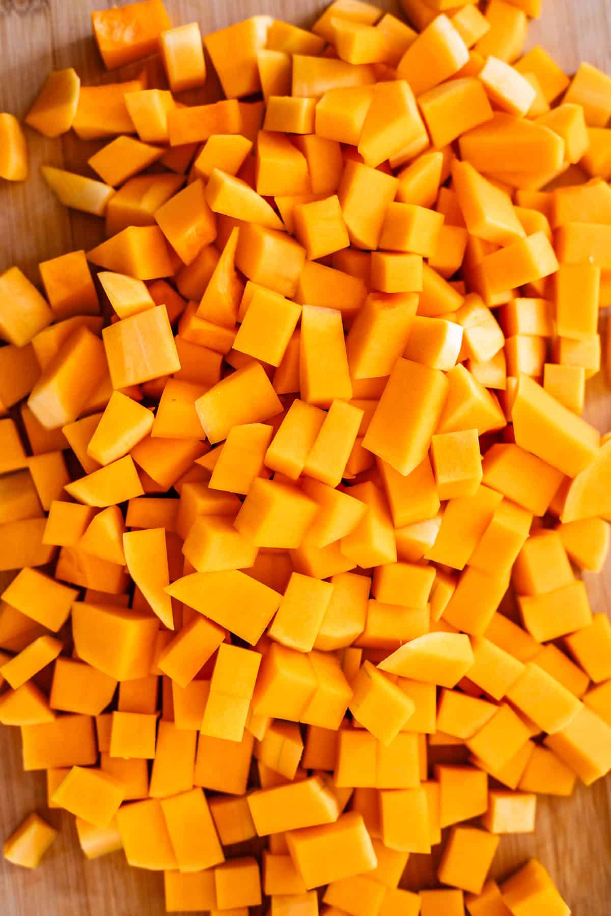 A pile of fresh, evenly diced orange butternut squash pieces spread out on a wooden cutting board.