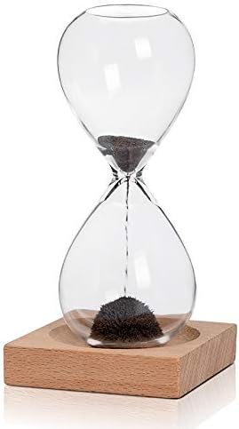 A glass hourglass filled with black sand sits on a square wooden base. The sand is partly collected in the bottom half and partially flowing through the narrow center.